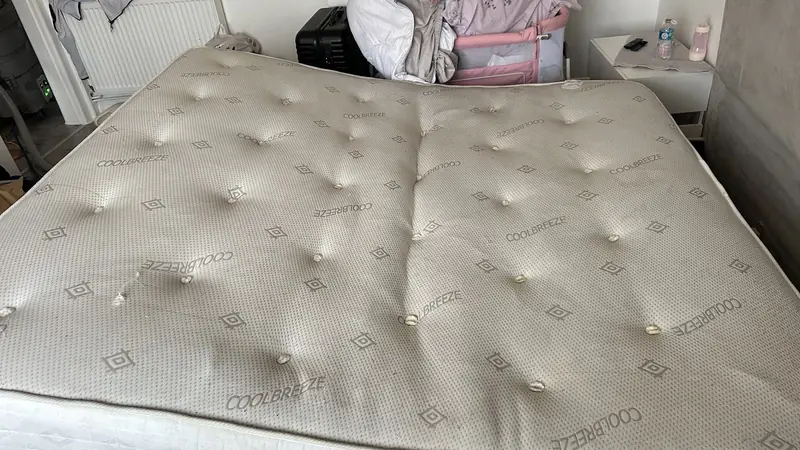 A quilted mattress on a bed frame before cleaning