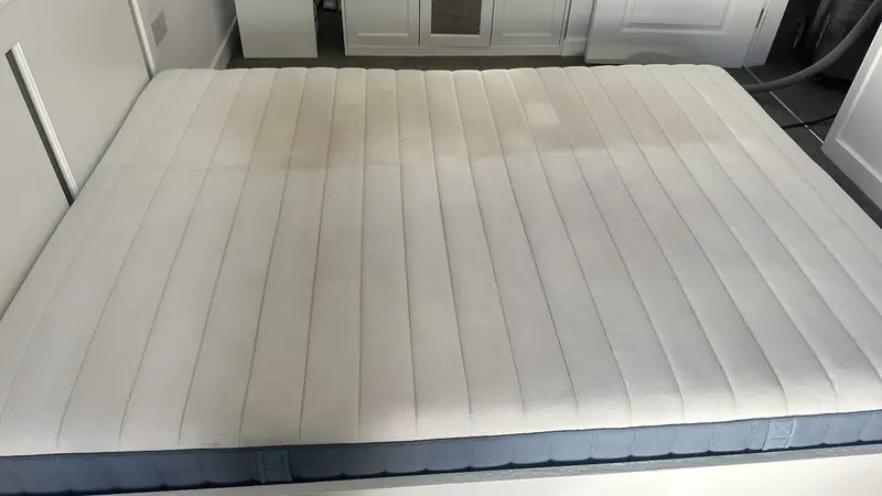 A mattress part-way through a steam clean, the cleaned half visibly brighter than the rest