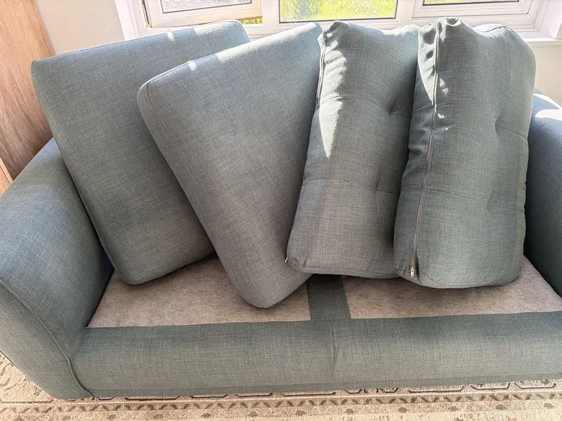 A grey sofa with its cushions stood up to dry after cleaning